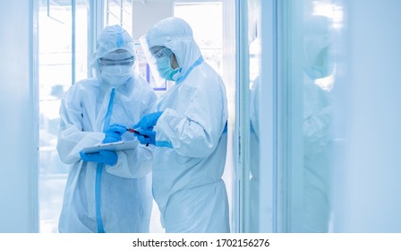 Two asian woman doctor in personal protective suit or PPE with mask writing on quarantine patient chart, holding test tube with blood sample for screening coronavirus. Coronavirus, covid-19 concept.