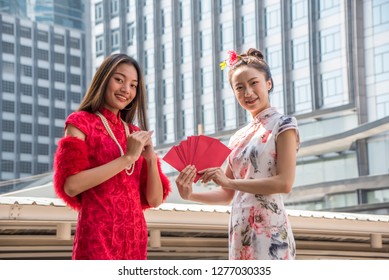 Two Asian woman in traditional chinese long dress, cheongsam, black hair, holding red envelope reward as a customer for Chinese New Year festival, celebration time.