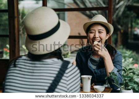 two asian woman travelers in hats sitting in japanese style old wooden house experience culture of sado. happy girl friends chatting laughing while eating sweet snacks drinking matcha green tea teien