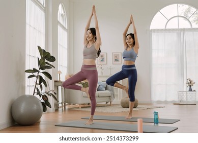 Two Asian woman wearing sportwear practicing yoga pose at home studio. Health care and wellness activities. - Powered by Shutterstock