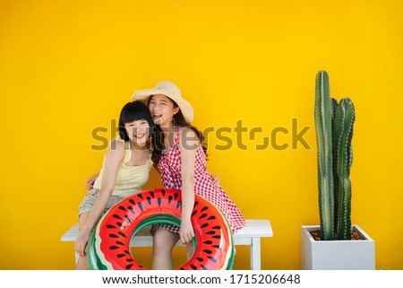Two asian women bestfriend closefriend on summer vacation. Traveling together on the beach. Over yellow background.