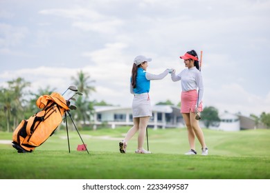 two asian women golfers congratulate high-five and happy smiling at golf course, with the golf bag next to them, sport women professional golfer concept, - Powered by Shutterstock