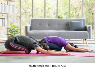 Two Asian Women Lay On Pink Exercise Mat Performing Yoga Child's Pose At Home. Clam Relaxation Harmony And Healthy Lifestyle.