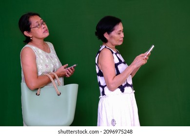 Two Asian Women Queuing Up; Bored Expression.