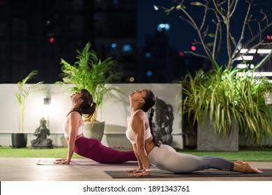 Two asian women in sportswear pants practicing yoga during city lockdown in their apratment with distance in background of cityscape illumination at night. Work out fitness healthy lifestyle concept. - Powered by Shutterstock