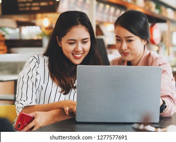 Two Asian women working with laptop together at co-working space.
