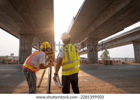 Two Asian worker engineer man and woman architect looking construction with white safety helmet in construction site. Standing at highway concrete road site. Work planning with blueprint and tablet.