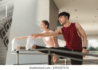 Two Asian young athlete man and woman in sportswear doing stretching together before jogging exercise in urban area. Warming up for workout outdoor in the morning. - Powered by Shutterstock