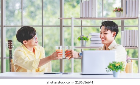 Two Asian Young Happy Pride Teenager Male Gay Men Lover Couple Partner Sitting Smiling Hugging Cuddling Together In Front Laptop Notebook Computer Browsing Surfing Using Credit Card Shopping Online.