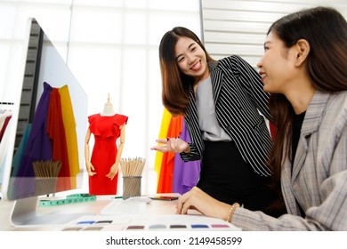 Two Asian Young Happy Success Female Stylish Fashion Designer Wears Casual Suit Talk Discuss Creative Design Information And Point At Computer Monitor Together In Front Of Clothes Rack And Mannequin.