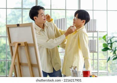 Two Asian Young Lovely Pride Teenager Male Gay Men Lover Couple Partner Standing Smiling Having Fun Playing Paintbrush In Front Canvas Painting Board On Easel In Glass Windows Workshop Studio At Home.