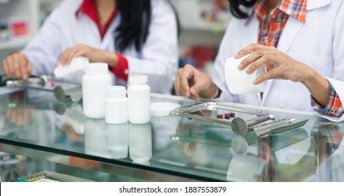 Two asian young woman pharmacist pour and count drug capsules on stainless tray, she prepare drug pack to patient in the pharmacy drugstore. Healthy and medicine concept. - Powered by Shutterstock
