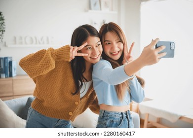Two asian young women happy smiling and taking selfie in living room at home. Video call, Meeting conference