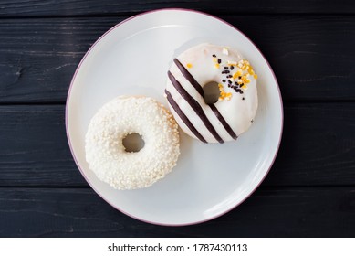Two assorted donuts on a small white plate with black background. Fresh sweet colorful homemade vanilla donuts on vintage background for birthday or party, top view, with free space for text