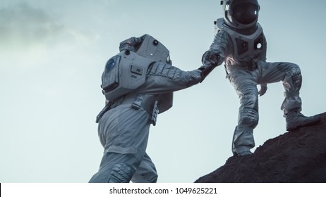 Two Astronauts Climbing Mountain Hill Helping Each Other, Reaching the Top. Overcoming Difficulties, Important Moment for the Human Race.