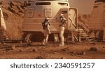 Two astronauts in spacesuits walk toward research station, colony or scientific base on Mars. Manned exploring space mission on red planet. Futuristic colonization and space exploration concept.