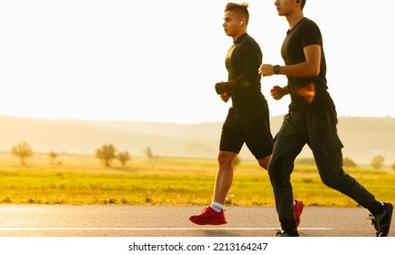 Two Athletes Running At Sunset. Backlit Silhouette Of Two Friends Training Together.