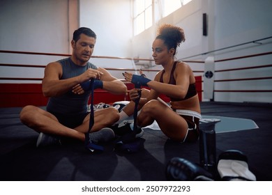 Two athletes wrapping hands with bandage while preparing for boxing training at health club. - Powered by Shutterstock