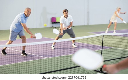 Two athletic men of different ages are playing a game of pickleball on a court inside a sports facility