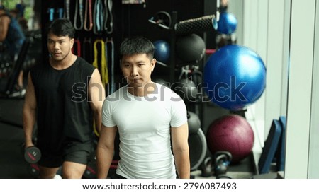 Two athletic men perform strength training exercises with dumbbells in a well-equipped fitness center.