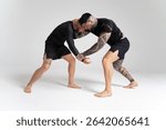 Two athletic men practicing wrestling on a white background, demonstrating grappling techniques in a studio setting