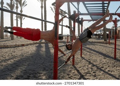 Two athletic men training on outdoor pull up bars on a sandy beach, doing advanced street workout skills like front lever and flag