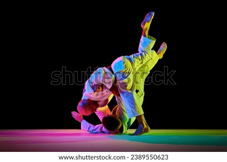 Two athletic, strong men, professional judokas, fighters showing their skills while competition in mixed neon light isolated black background. Concept of martial art, combat sport, health, energy. Ad