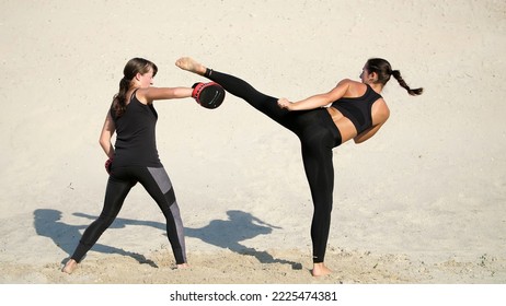 Two athletic, young women in black fitness suits are engaged in a pair, work out kicks, on a deserted beach, against a blue sky, in the summer, under a hot sun. Slow motion. High quality photo - Powered by Shutterstock