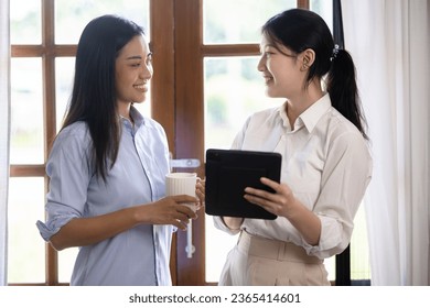Two attractive Asian women holding a digital tablet and talking with friends at home, Two ideas woman. - Shutterstock ID 2365414601