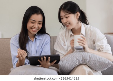 Two attractive Asian women using digital tablet with friends sitting on sofa at home. - Shutterstock ID 2365414615