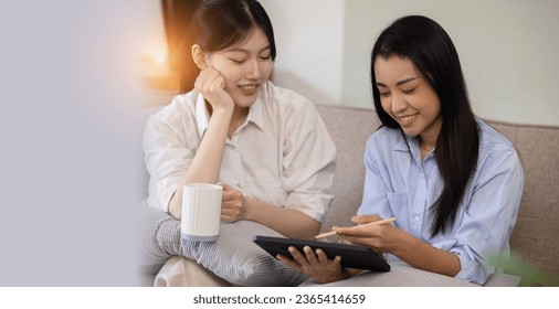 Two attractive Asian women using digital tablet with friends sitting on sofa at home. - Shutterstock ID 2365414659