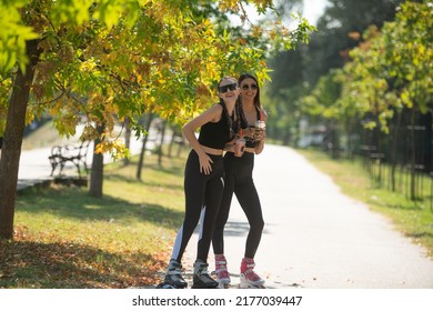 Two attractive best friends talking and drinking smoothies in the park while standing on their rollerskates