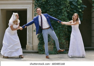 Two Attractive Brides Dragging And Pulling The Groom With His Hands