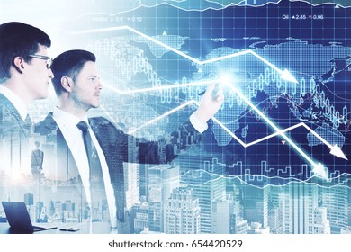 Two attractive businessmen drawing downward forex chart arrows on city background. Sales concept. Double exposure