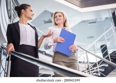 Two Attractive Bussiness Women Moving Down The Stairs And Talking.