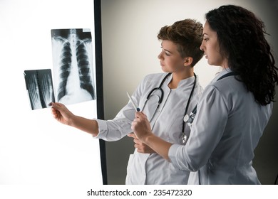 X-ray를 보고 있는 두 명의 매력적인 의사들은 회색 배경에 결과를 봅니다 스톡 사진