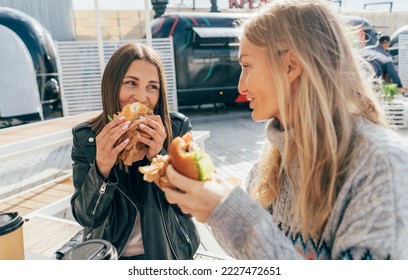 Two attractive European women eat street fast food while sitting at a table outside. - Powered by Shutterstock