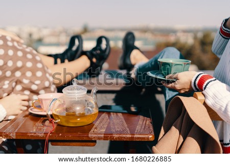 Two attractive girls enjoy a tea party on the rooftop overlooking the city. Drinking healthy buckwheat tea. Healthcare or herbal medicine concept. Close-up on mugs
