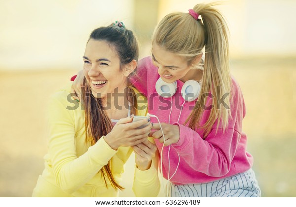 Two attractive and\
sporty girl friends relaxing with cellphone after running. Living\
healthy lifestyle.