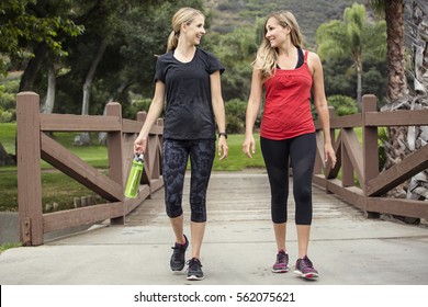Two attractive women in their 30s talking a walk or jog together in the outdoors. Cute blond and fit women who are active and working to stay healthy. 