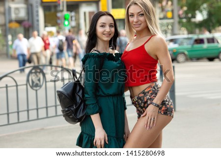 Two attractive young girl friends standing together and posing on camera.Brunette and blonde having fun.