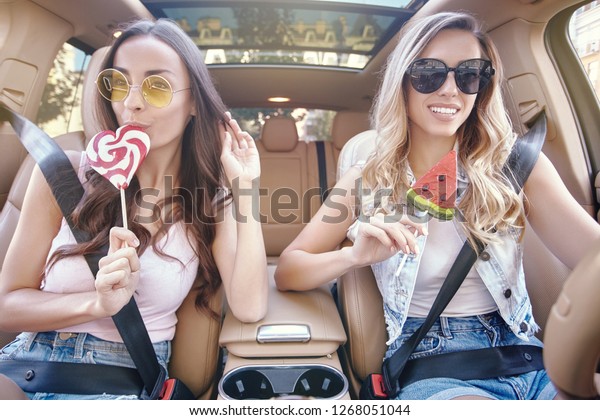 two attractive young women eating big lollipops in\
luxury car