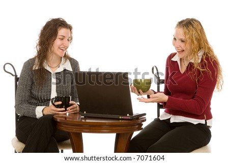 Two attractive young women sitting at a cafe table and sharing a laugh at an e-mail or instant message over a cup of coffee.