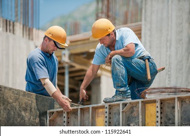 Two authentic construction workers collaborating in the installation of concrete formwork frames