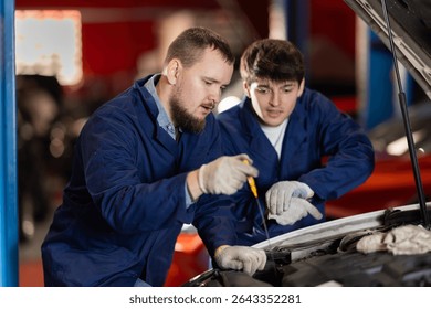 Two auto mechanics checking engine oil level under the hood of car together in a garage
