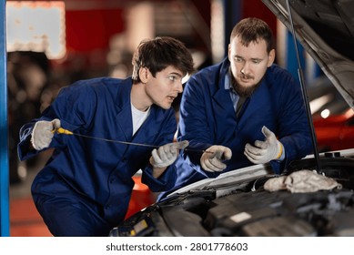 Two auto mechanics checking engine oil level under the hood of car together in a garage