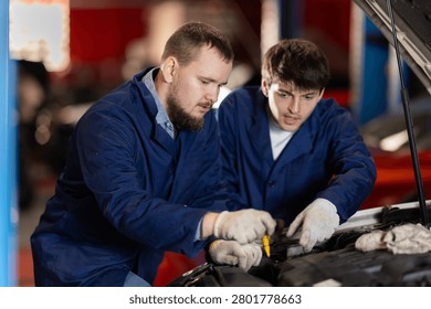 Two auto mechanics checking engine oil level under the hood of car together in a garage