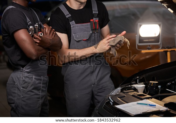 two auto mechanics discuss problems of repairing\
a car, stand talking,\
cropped