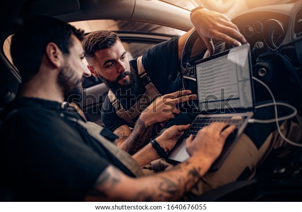 Two auto mechanics doing diagnostics\
with laptop.Car service, repair and people\
concept.