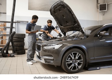 Two auto mechanics inspecting car engine in workshop environment. Professionals diagnosing vehicle with laptop and tools. Automotive maintenance, repair, and teamwork concept - Powered by Shutterstock